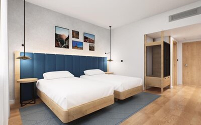 Guest room with two beds, blue padded headboard, wood furniture, and framed wall artwork