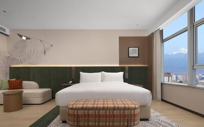 King bedroom with mountain and city views through corner windows, chaise lounge, and patterned bench