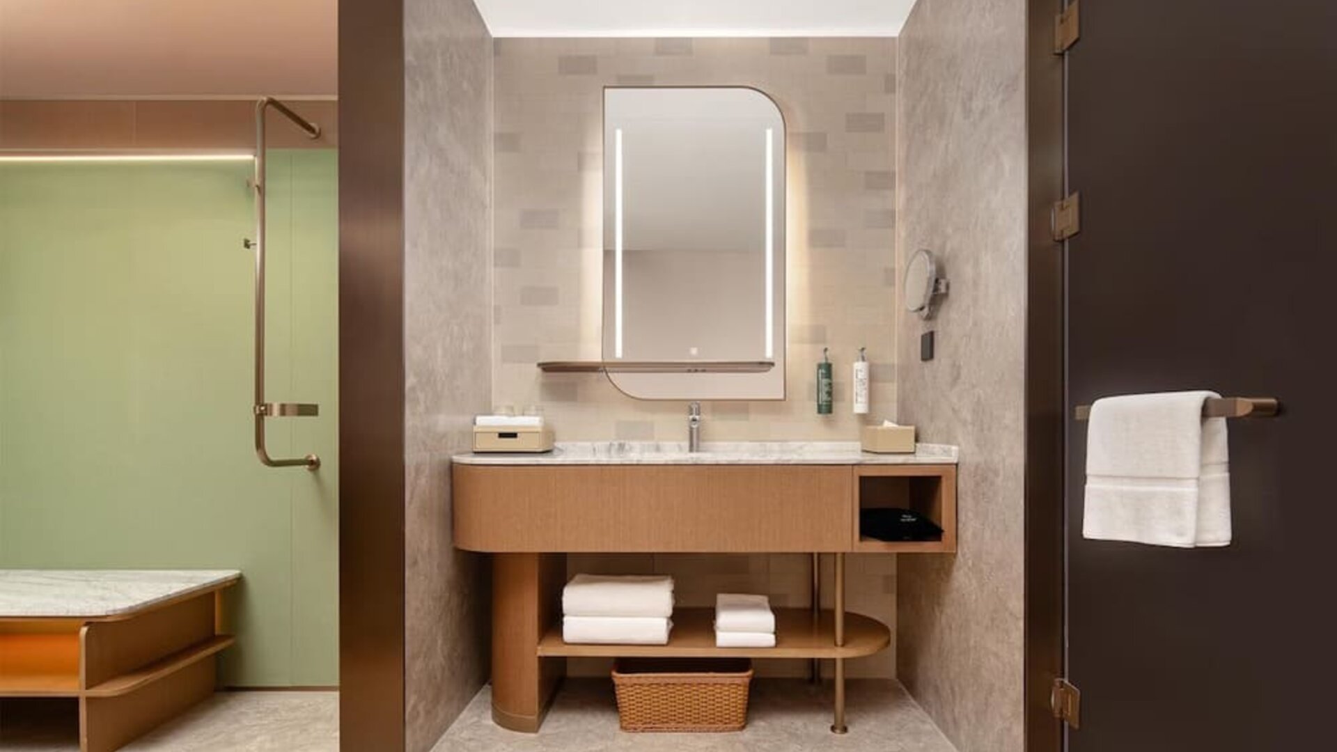 Modern bathroom vanity with illuminated mirror, marble counter, towels, and glass shower entrance