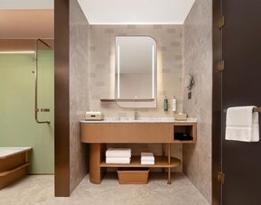 Modern bathroom vanity with illuminated mirror, marble counter, towels, and glass shower entrance