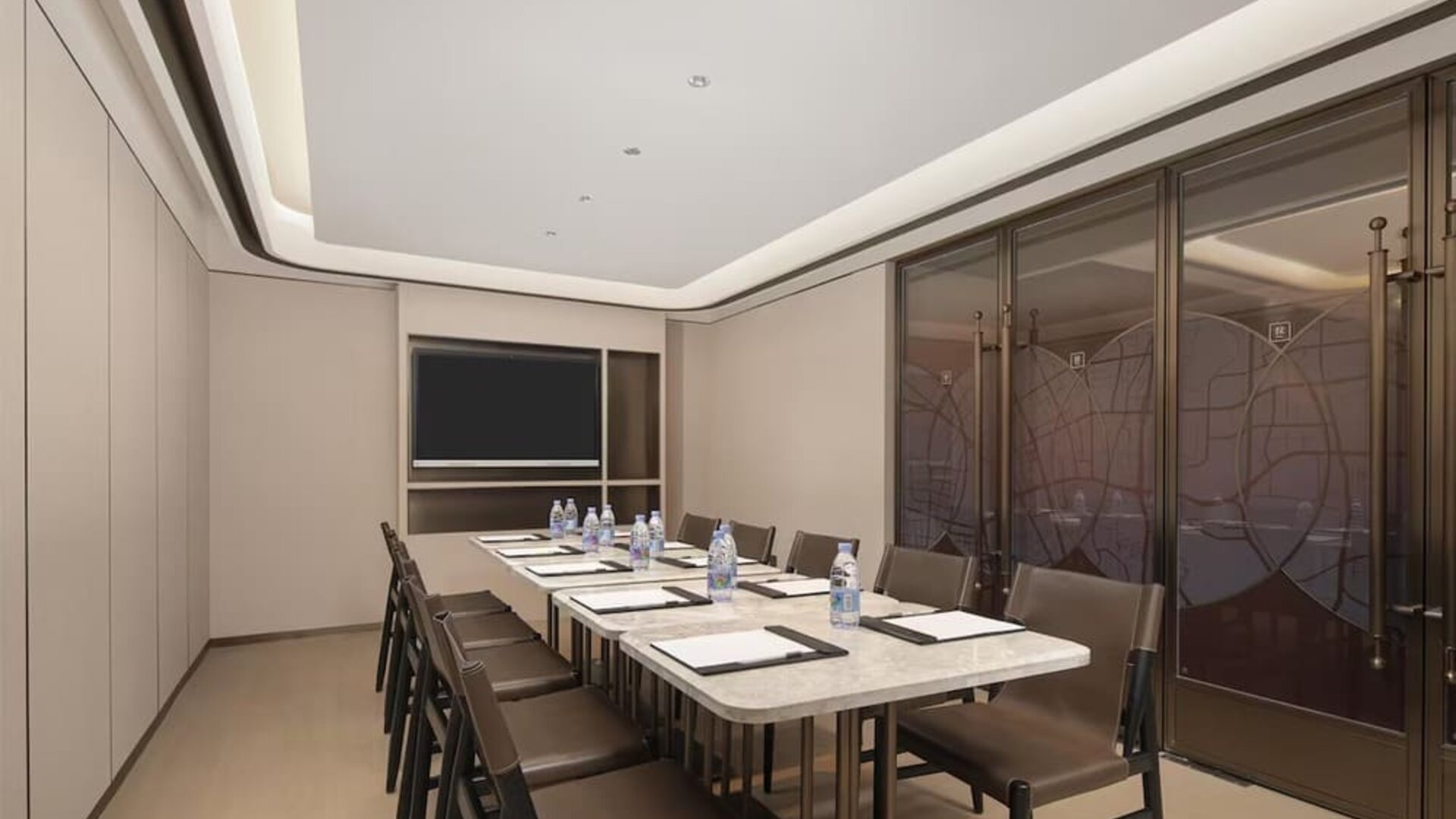 Narrow meeting room with marble conference table, leather chairs, bottled water, and wall-mounted TV