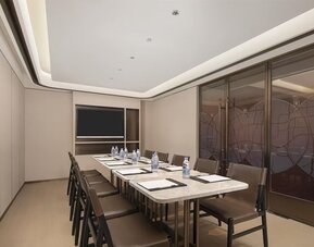 Narrow meeting room with marble conference table, leather chairs, bottled water, and wall-mounted TV