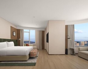 King bedroom with mountain and city views through corner windows, chaise lounge, and patterned bench