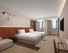 Modern double room with two beds, orange headboards, seating area, and floor-to-ceiling windows