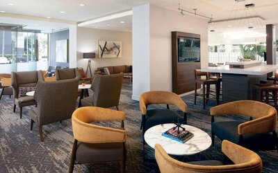 Lobby seating area with contemporary armchairs, marble tables, and warm neutral décor at Courtyard By Marriott Los Angeles LAX/Century Boulevard.