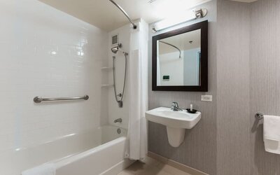 Accessible bathroom with bathtub, grab bars, wall-mounted sink, and modern neutral finishes at Courtyard By Marriott Los Angeles LAX/Century Boulevard.