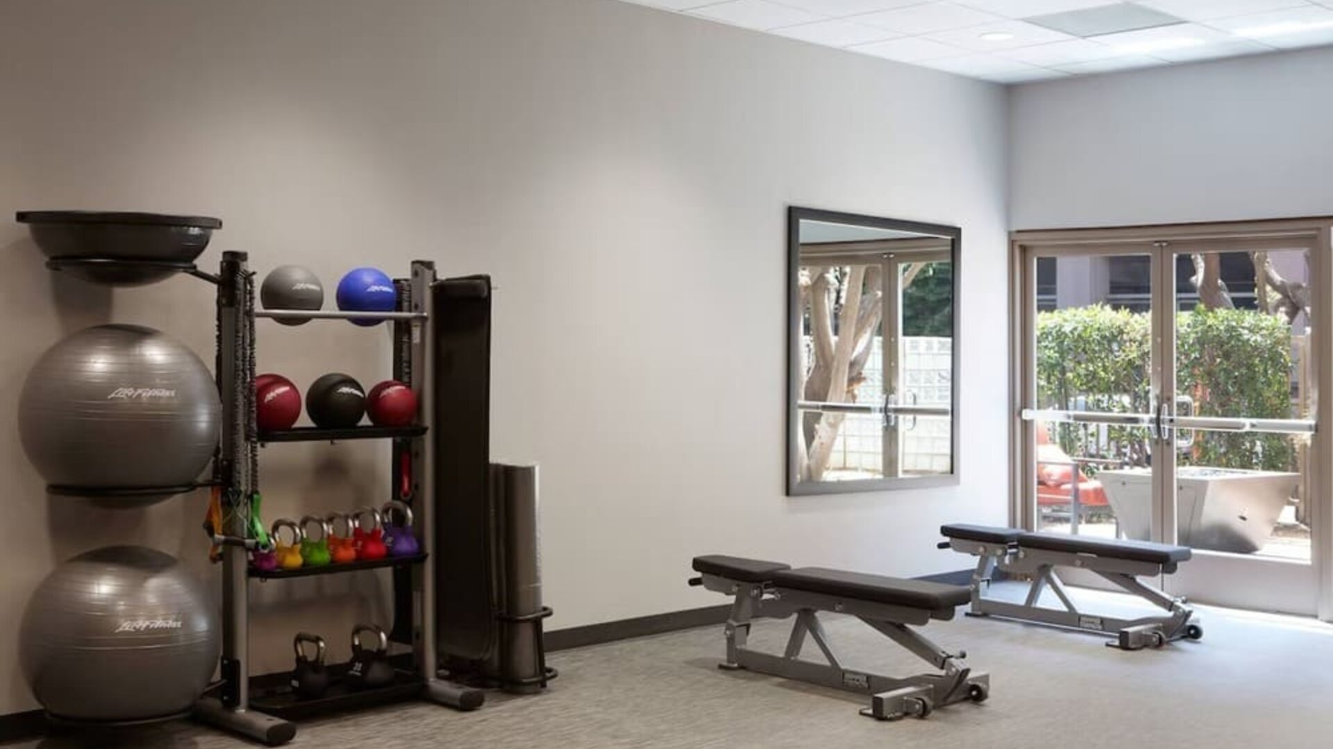 Bright fitness facility with benches, free weights, exercise balls, and outdoor-facing windows at Courtyard By Marriott Los Angeles LAX/Century Boulevard.