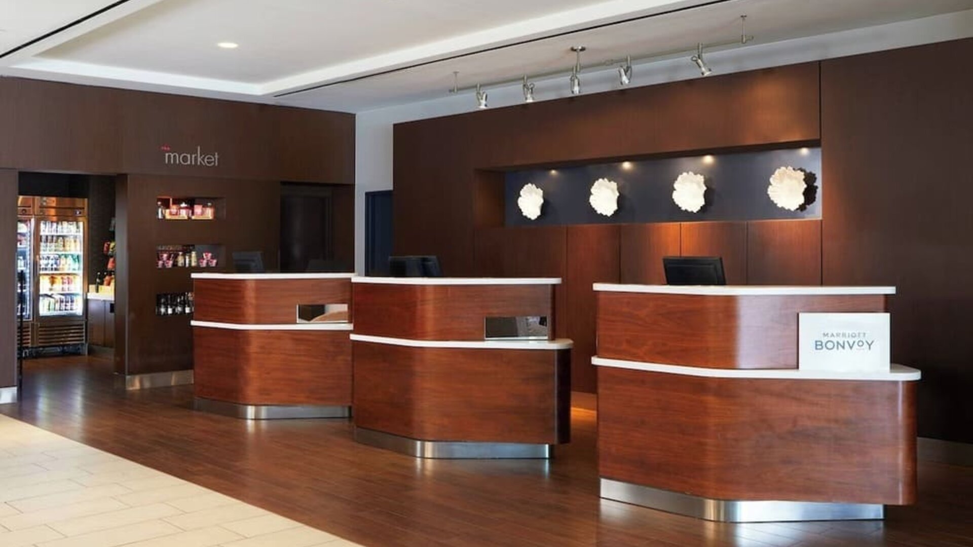 eception desk area with wood finishes, Marriott Bonvoy branding, and adjacent market/snack section at Courtyard By Marriott Los Angeles LAX/Century Boulevard.