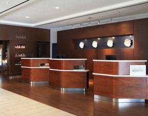 eception desk area with wood finishes, Marriott Bonvoy branding, and adjacent market/snack section at Courtyard By Marriott Los Angeles LAX/Century Boulevard.