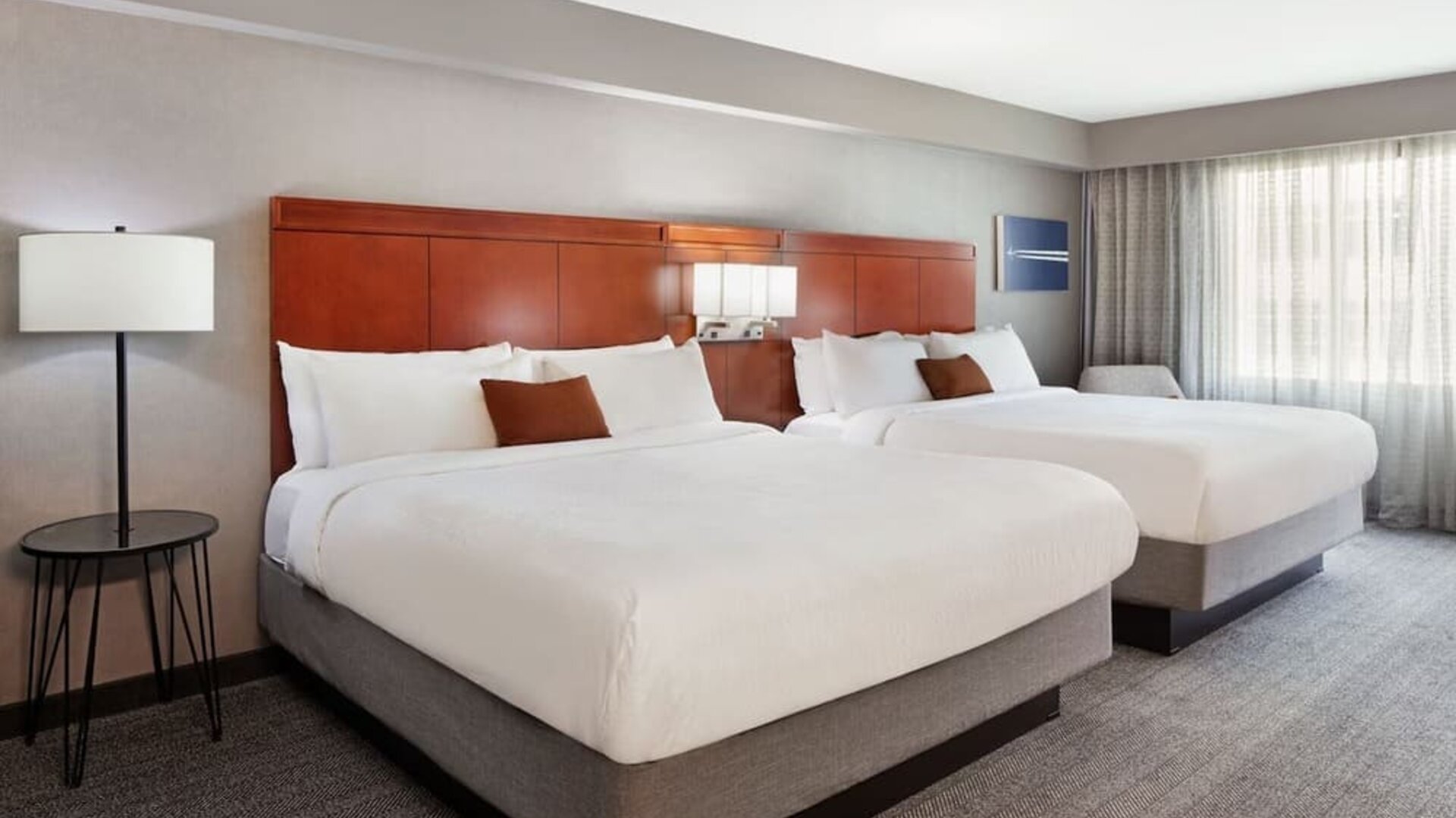 Spacious double queen guest room with modern furnishings, wood headboards, and soft natural lighting at Courtyard By Marriott Los Angeles LAX/Century Boulevard.