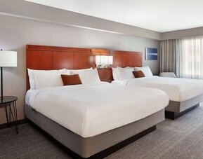 Spacious double queen guest room with modern furnishings, wood headboards, and soft natural lighting at Courtyard By Marriott Los Angeles LAX/Century Boulevard.