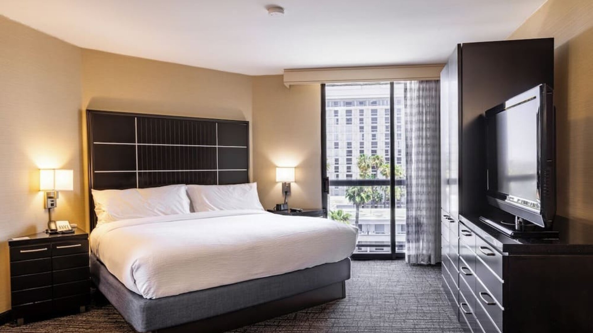 King guest room with floor-to-ceiling window, large TV cabinet, and contemporary furnishings at Embassy Suites By Hilton LAX Airport North.