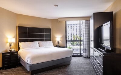 King guest room with floor-to-ceiling window, large TV cabinet, and contemporary furnishings at Embassy Suites By Hilton LAX Airport North.