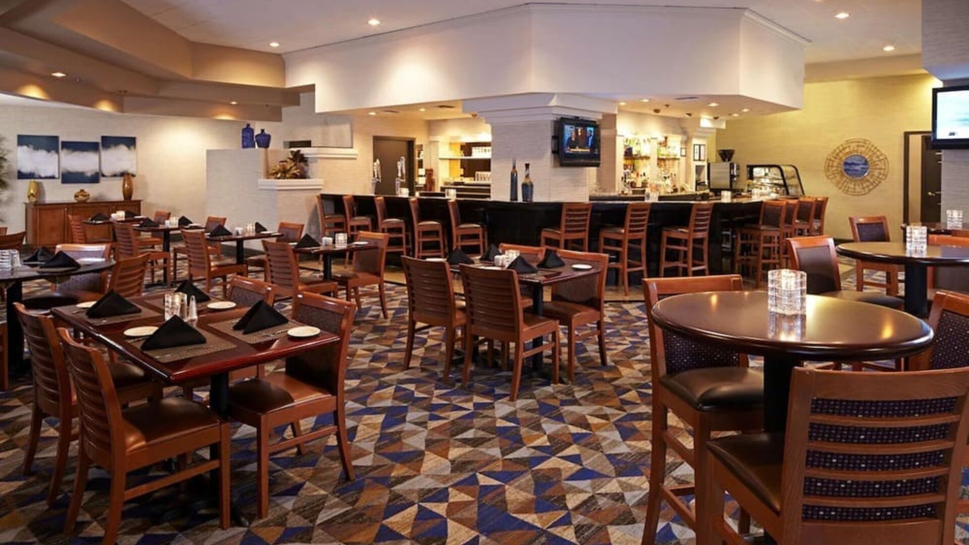 Spacious dining area with restaurant seating, patterned carpet, and central bar area at Embassy Suites By Hilton LAX Airport North.