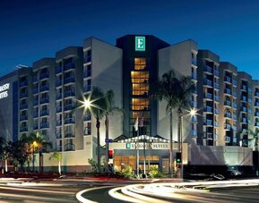 Evening exterior view of the hotel building with lit windows and palm-lined street at Embassy Suites By Hilton LAX Airport North.