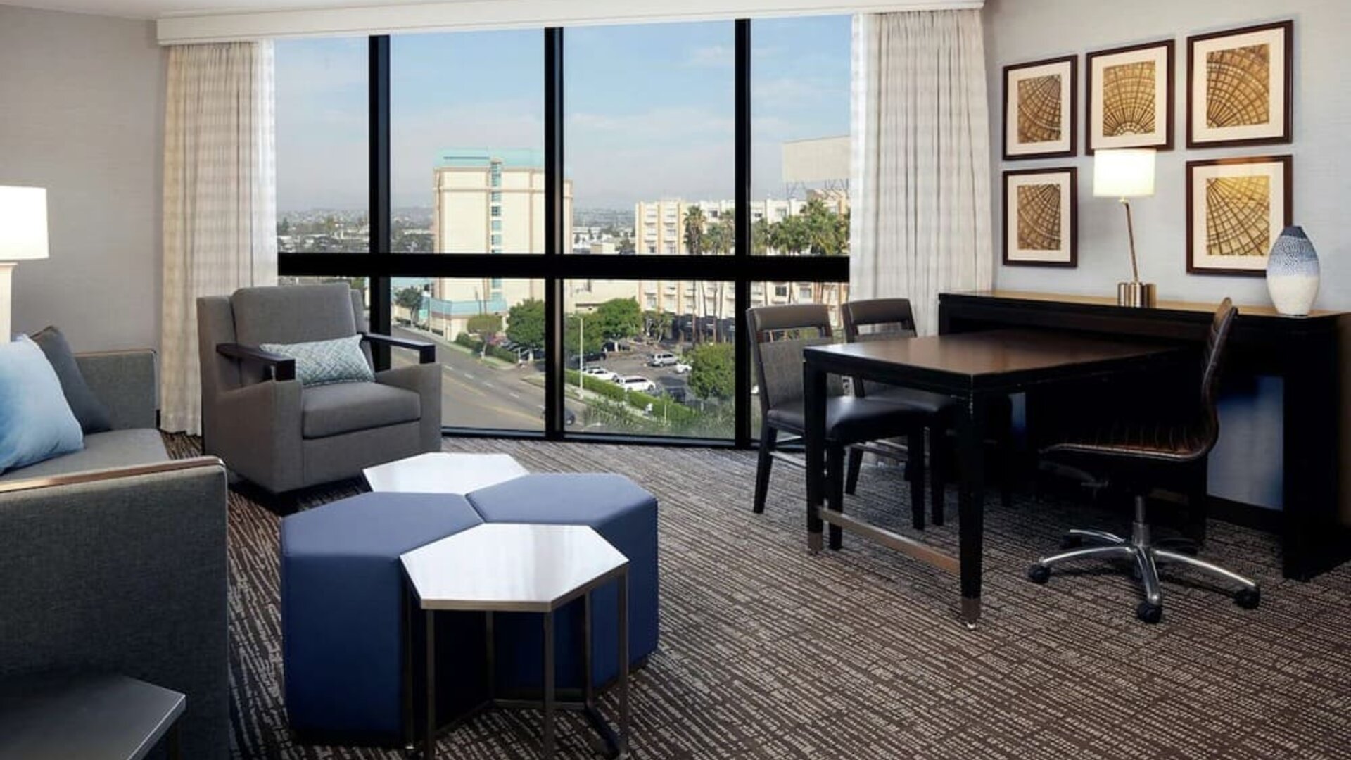 Spacious suite living area with city views, dining table, lounge seating, and floor-to-ceiling windows at Embassy Suites By Hilton LAX Airport North.