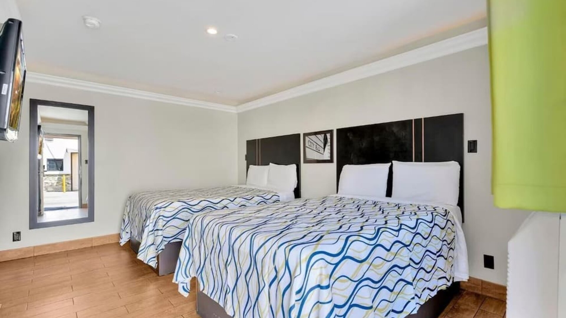 Guest room with two double beds, tiled flooring, modern lighting, and wall-mounted TV at Mid City Inn - Los Angeles.