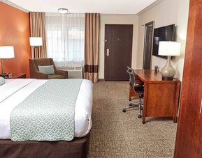 King guest room with work desk, armchair, large window, and warm orange accent wall at The Hills Inn Eagle Rock.