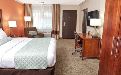 King guest room with work desk, armchair, large window, and warm orange accent wall at The Hills Inn Eagle Rock.