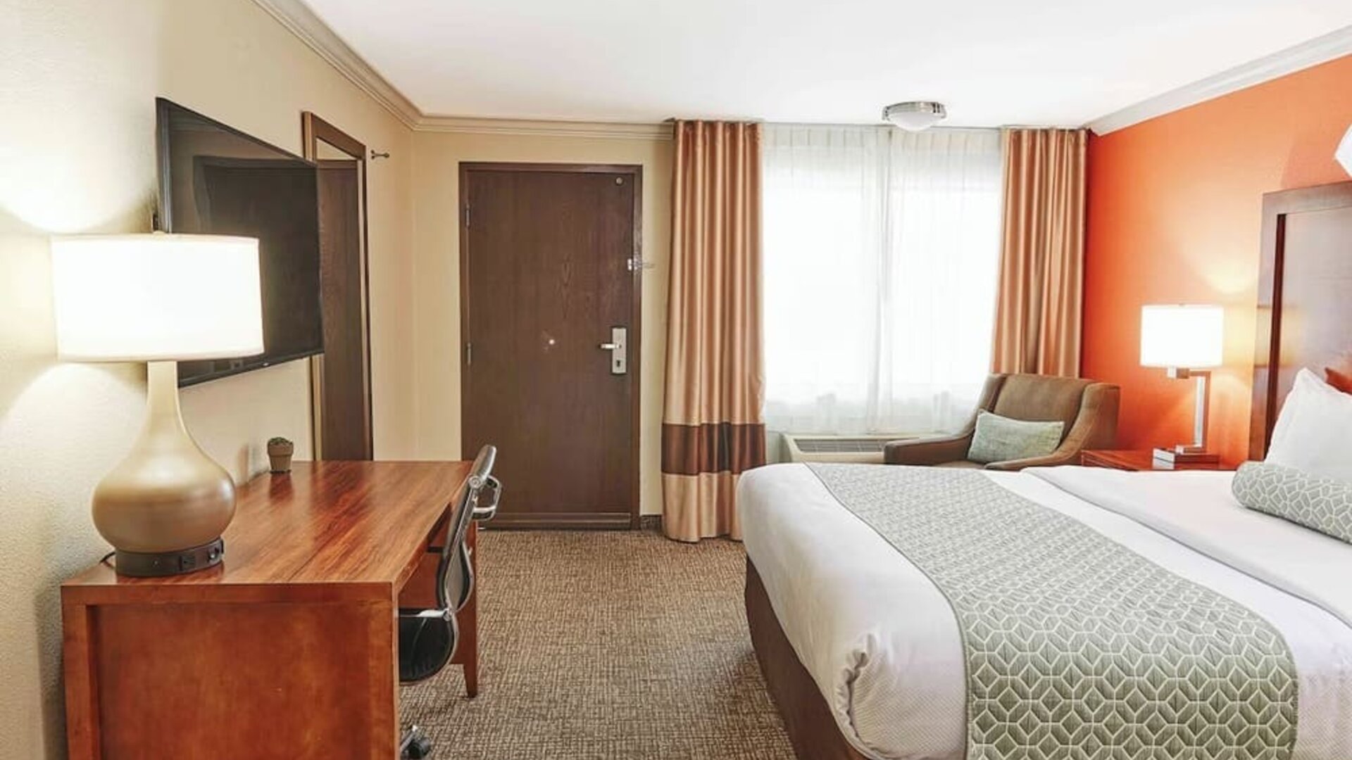 Guest room with king bed, work desk, upholstered chair, and large curtained window at The Hills Inn Eagle Rock.