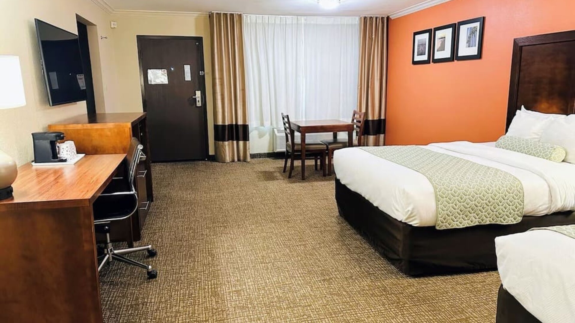 Spacious guest room with two beds, work desk, dining table, and orange accent wall at The Hills Inn Eagle Rock.