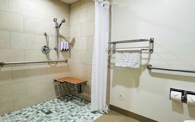 Accessible bathroom with roll-in shower, grab bars, fold-down bench, and tiled flooring at The Hills Inn Eagle Rock.