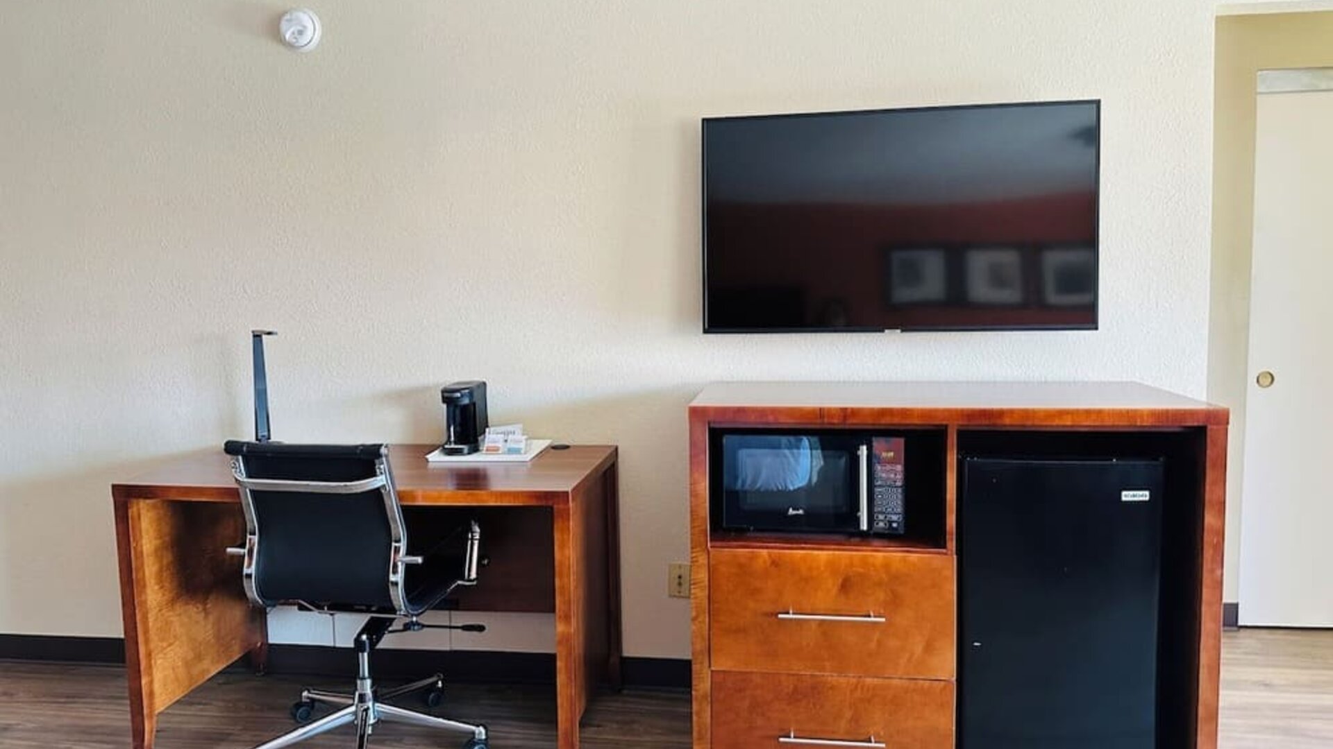 Work area with desk chair, flat-screen TV, microwave, mini fridge, and wood flooring at The Hills Inn Eagle Rock.