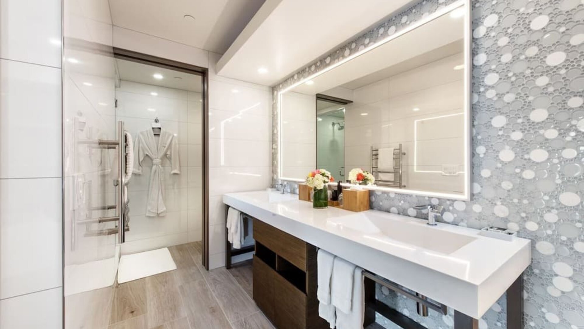 Modern bathroom with double vanity, illuminated mirror, walk-in shower, and patterned wall tiles at Shade Hotel Manhattan Beach.