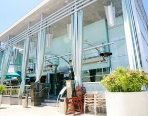 Hotel entrance with floor-to-ceiling windows, outdoor seating, and decorative white drapes at Shade Hotel Manhattan Beach.