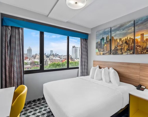 Spacious guest room with large bed, skyline artwork, yellow chair, and expansive city views at Days Inn Chinatown NYC.