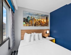 Bright guest room with queen bed, skyline canvas art, and corner city-view windows at Days Inn Chinatown NYC.