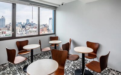 Small dining area with round tables, wooden chairs, and panoramic city skyline views at Days Inn Chinatown NYC.