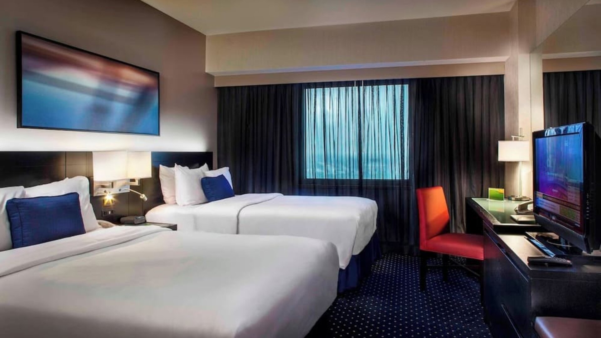 Spacious guest room with two beds, workspace, and city-style décor at Courtyard By Marriott New York JFK Airport.