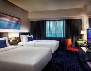 Spacious guest room with two beds, workspace, and city-style décor at Courtyard By Marriott New York JFK Airport.