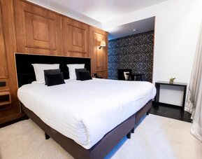 King bedroom with elegant wood finishes and seating nook at Hôtel Espérance.