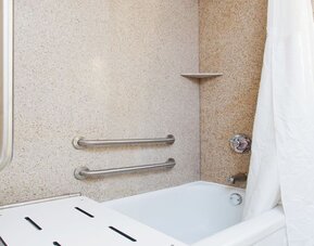 Accessible bathroom with bathtub, safety grab bars, and transfer bench at Holiday Inn Downtown Shreveport.