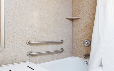 Accessible bathroom with bathtub, safety grab bars, and transfer bench at Holiday Inn Downtown Shreveport.