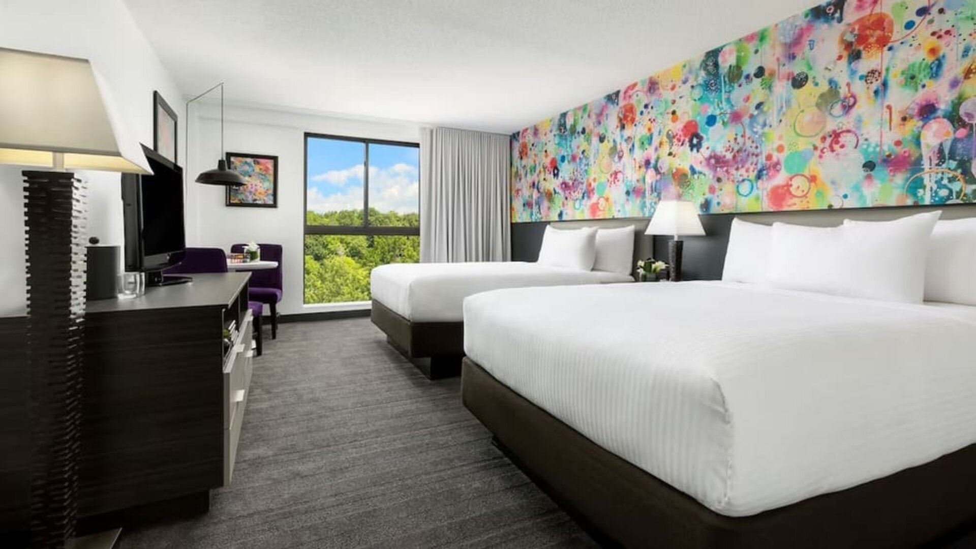 Double queen guest room with vibrant artistic décor and natural light at Hotel Studio Allston.