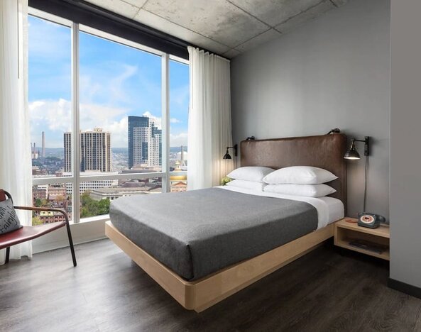 Guest room with platform bed and floor-to-ceiling windows overlooking the Boston skyline at Moxy Boston Downtown.