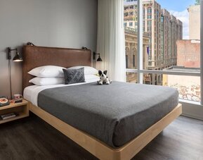 Guest room with leather headboard and large corner windows overlooking downtown Boston at Moxy Boston Downtown.