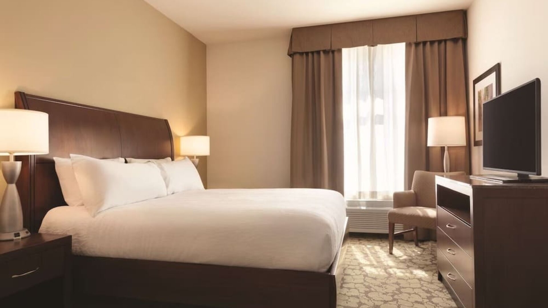 Guest room with king bed, TV, armchair, and window with blackout curtains at Hilton Garden Inn Boston Logan Airport.