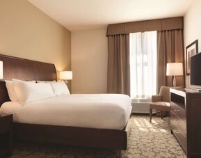 Guest room with king bed, TV, armchair, and window with blackout curtains at Hilton Garden Inn Boston Logan Airport.