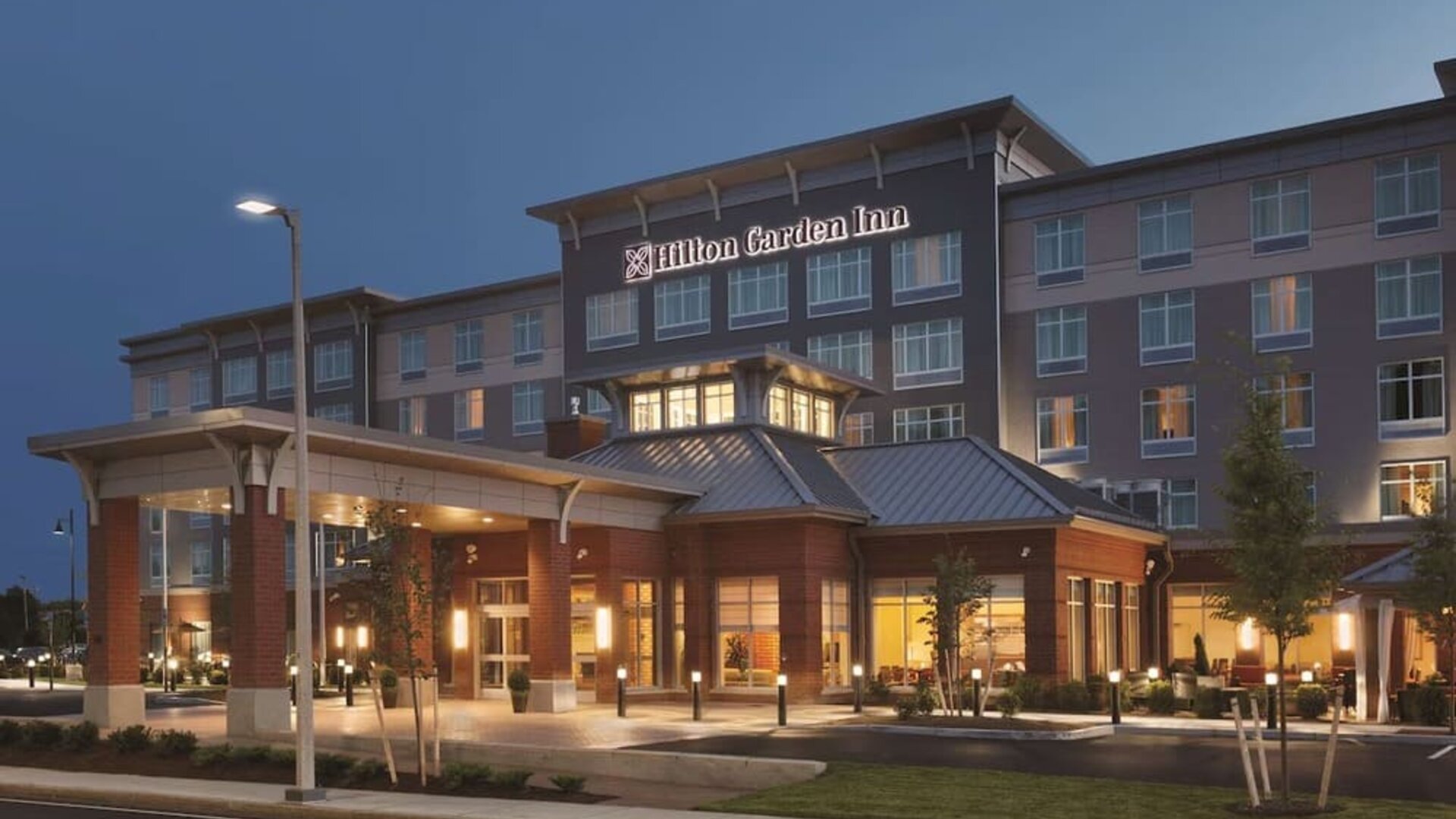 Evening exterior view of Hilton Garden Inn Boston Logan Airport with illuminated entrance and porte cochère.