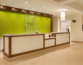 Hotel reception desk with illuminated green accent wall and modern lobby lighting at Hilton Garden Inn Boston Logan Airport.