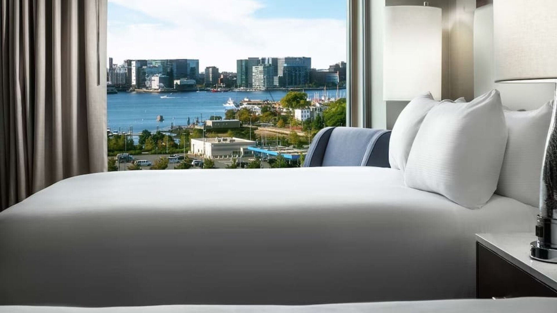 Bed positioned beside large window with harbor and city skyline view at Hilton Boston Logan Airport.