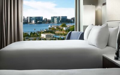 Bed positioned beside large window with harbor and city skyline view at Hilton Boston Logan Airport.