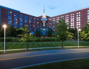 Evening exterior view of Hilton Boston Logan Airport surrounded by landscaped grounds and roadway lighting.