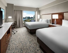 Room with two beds, workspace desk, and waterfront city view through large window at Hilton Boston Logan Airport.