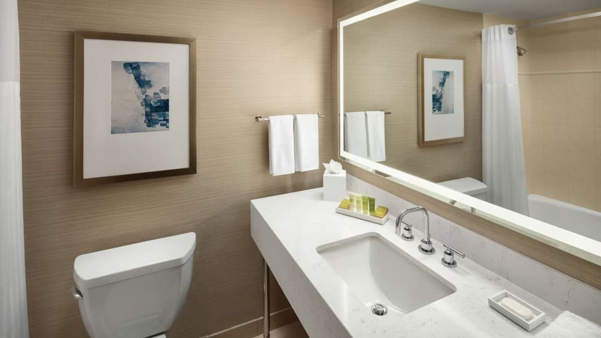 Modern bathroom with illuminated mirror, white vanity countertop, and bathtub shower combo at Hilton Boston Logan Airport.
