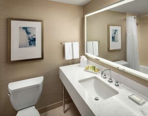 Modern bathroom with illuminated mirror, white vanity countertop, and bathtub shower combo at Hilton Boston Logan Airport.